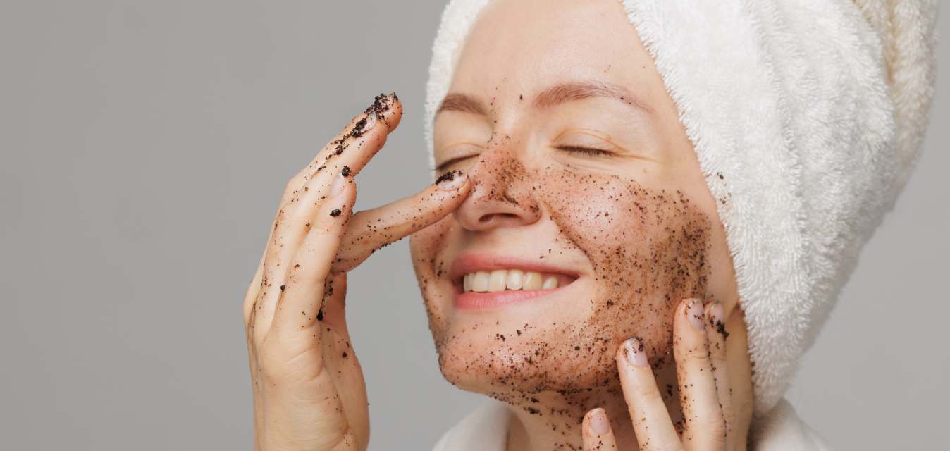 Frau mit Handtuch im Haar trägt ein Gesichtspeeling auf und massiert sanft ihre Haut.