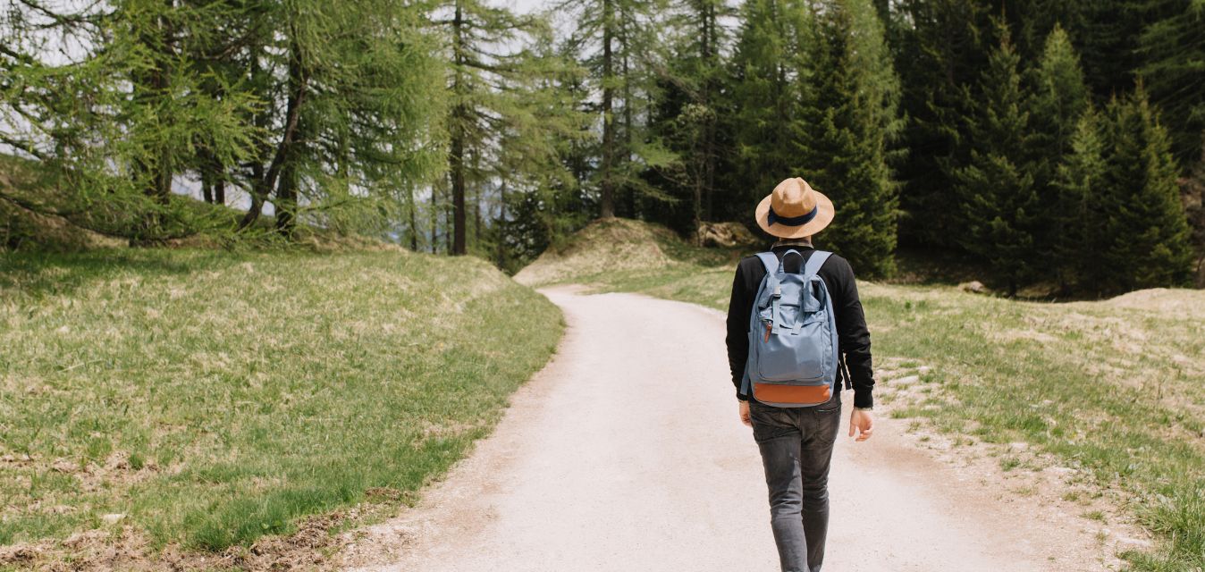 Mensch mit Hut, der auf einen Wald zuläuft.
