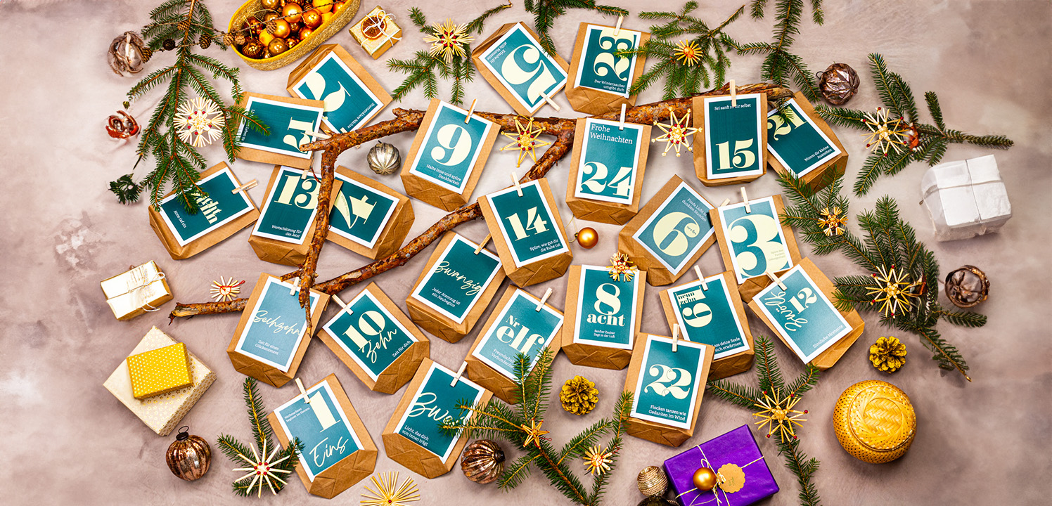 Adventskalender aus braunen Tüten und gelb grünen Zahlen. Als Dekoration gibt es einen flauschigen teppich, Geschenke und geschmückte Tannenzweige.