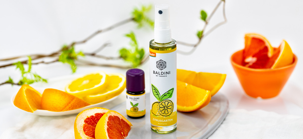 Baldini Zitrusgarten Raumspray und ätherisches Zitrusöl, dekoriert mit frischen Orangen-, Zitronen- und Grapefruitstücken sowie grünen Zweigen.