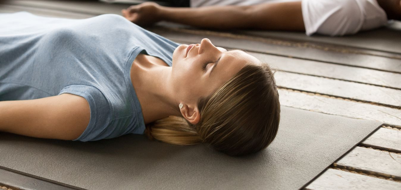 Frau liegt entspannt mit geschlossenen Augen auf einer Yogamatte während einer Ruhe- oder Entspannungseinheit.