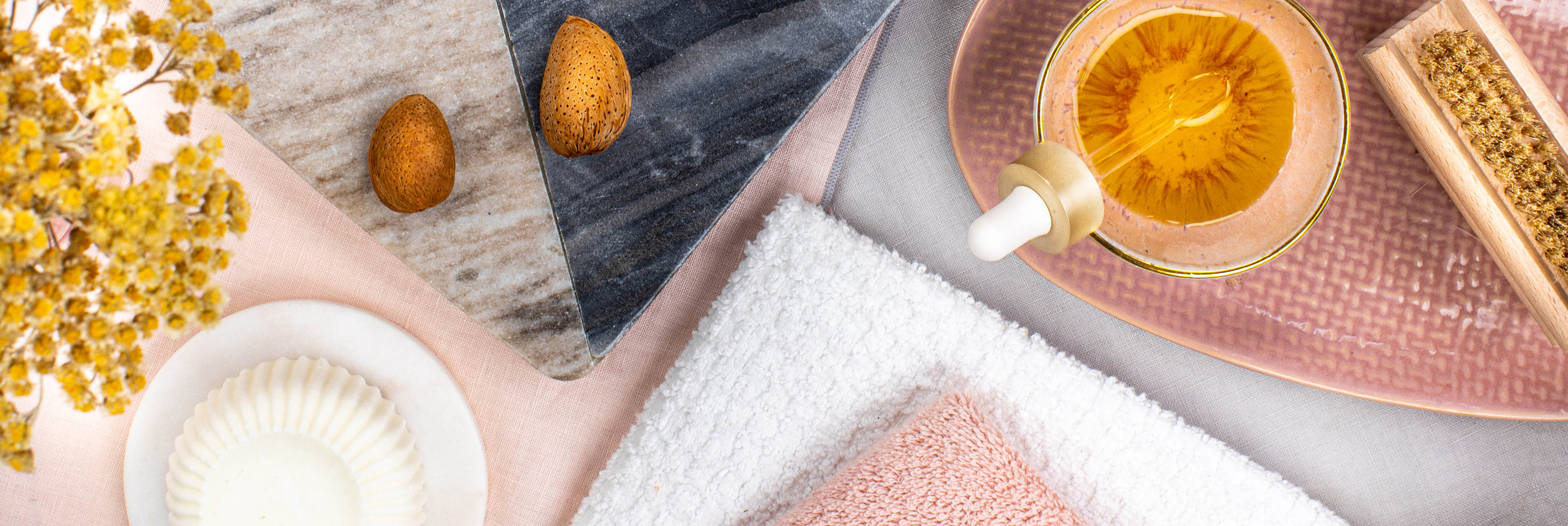 Ein Tisch dekoriert mit Wellness Elementen und einer kleinen Glasschüssel mit gelb-goldenen Öl. 