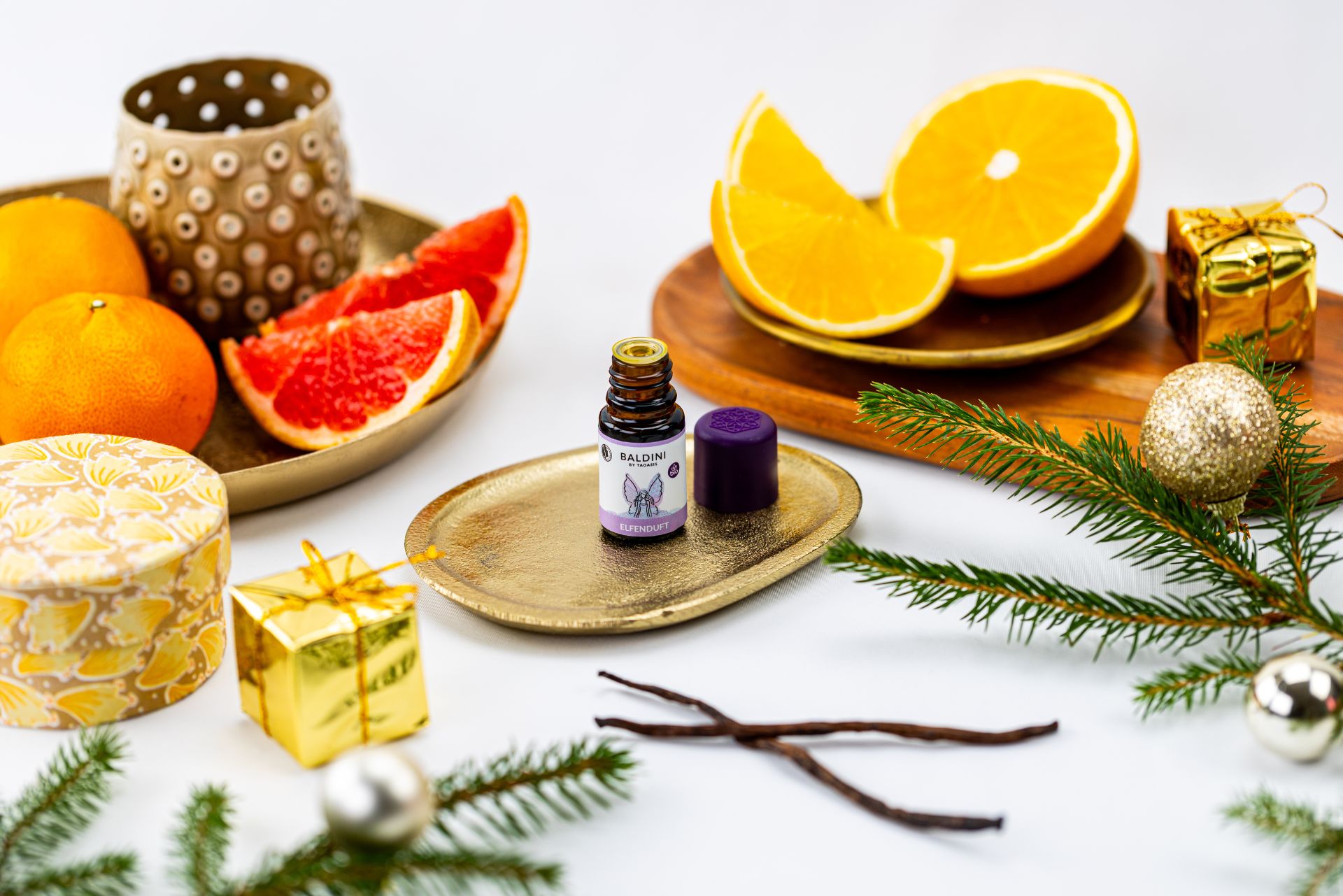 Duftkomposition Elfenduft vor weihnachtlichem Hintergrund mit Obst wie Orangen, Pampelmusen. Daneben liegen Zweige und Weihnachrtsdeko.