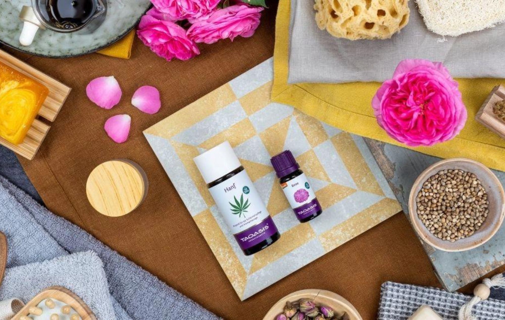 Sinnliches Körperpflegeöl mit Hanföl und Rose, umgeben von Blüten, Samen und natürlichen Spa-Accessoires dekorativ arrangiert