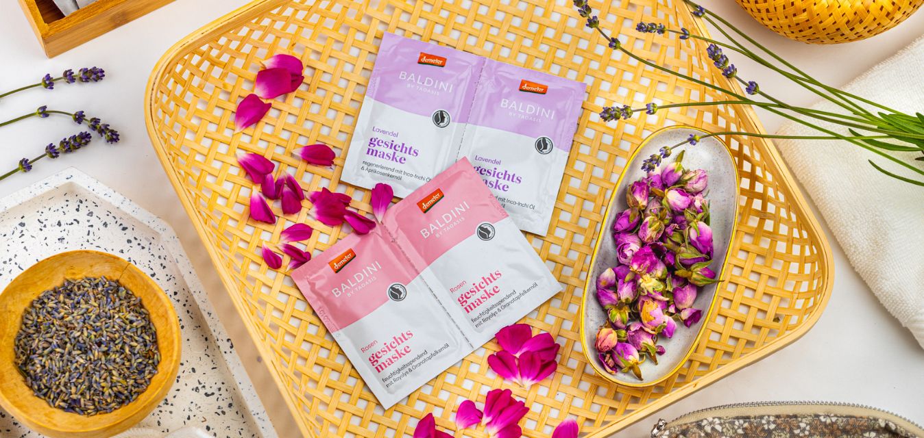 Baldini Gesichtsmasken Rose und Lavendel dekorativ mit Blüten, Lavendel und Rosenknospen arrangiert.