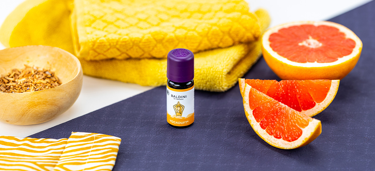 Baldini Yogaduft Duftkomposition mit frischer Grapefruit, gelbem Handtuch und natürlichen Zutaten dekorativ arrangiert.