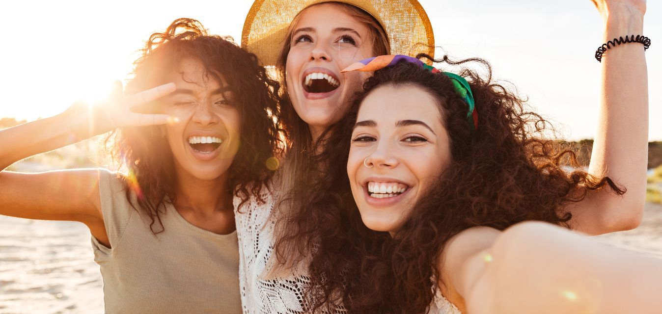 Drei junge Frauen lachen und machen ein Selfie im Sonnenlicht.