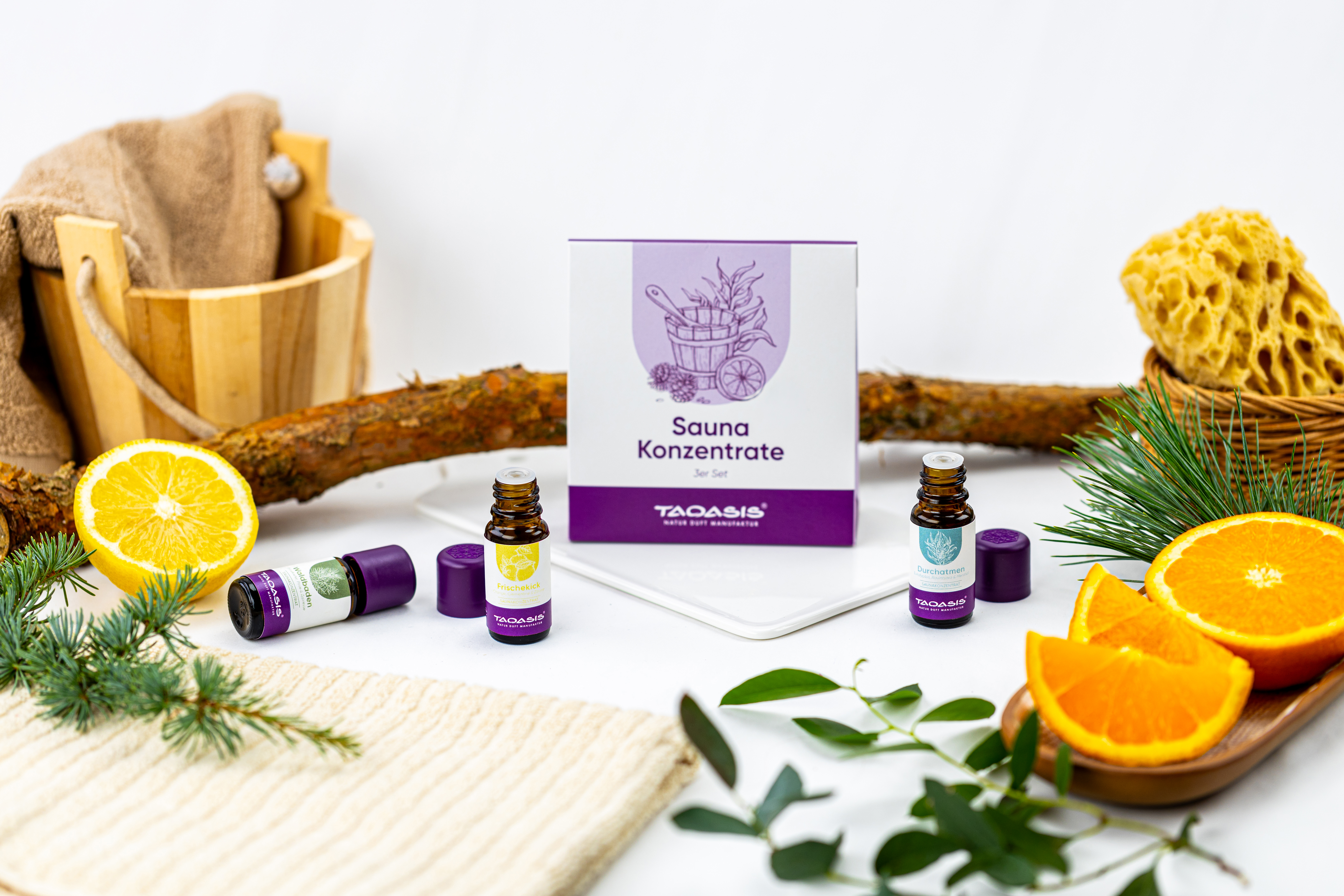 TAOASIS Saunakonzentrate 3er Set mit kleinen Duftfläschchen, Zitrusfrüchten, Tannenzweigen und Sauna-Accessoires dekorativ arrangiert.
