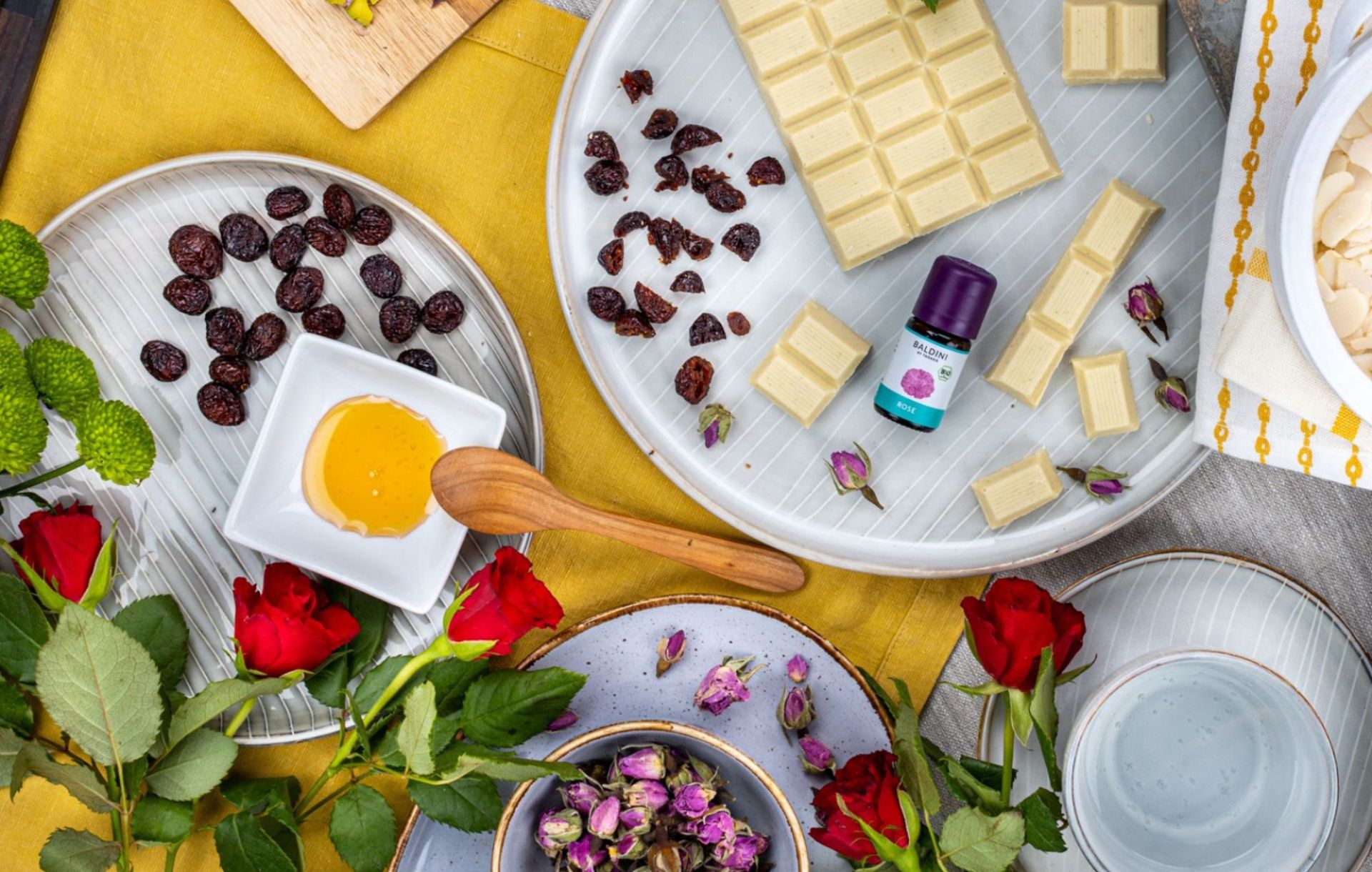 Weiße Schokolade, Rosinen und Mandeln mit Honig, Rosenblüten und ätherischem Rosenöl dekorativ angerichtet.