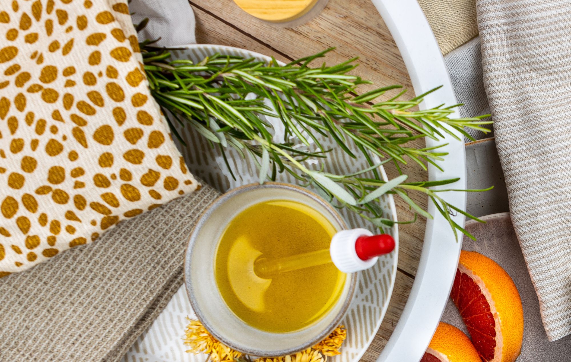 Sportliches Massageöl mit Pipette, umgeben von Rosmarin, Grapefruit und natürlichen Stoffen auf Tablett arrangiert