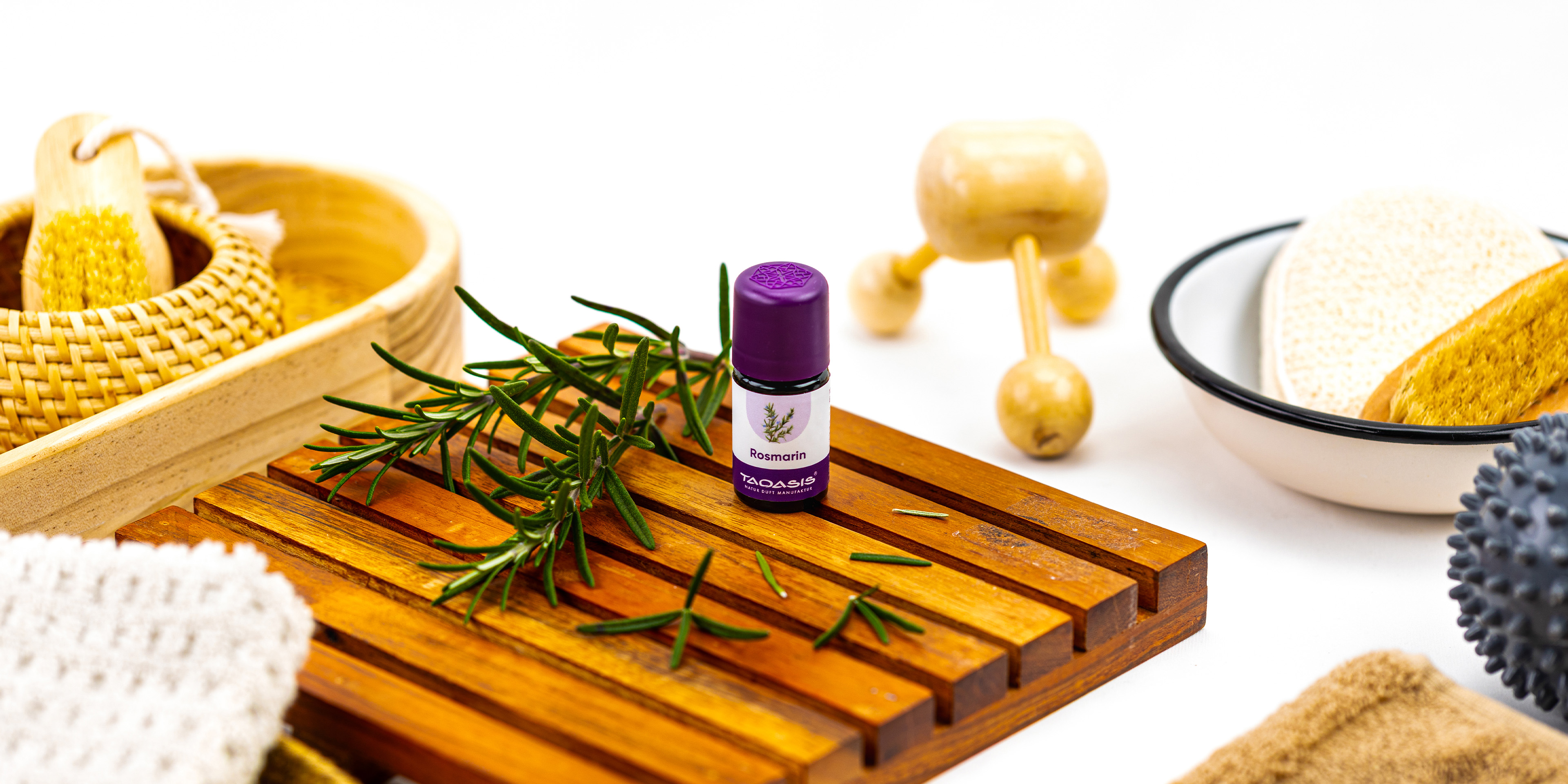 TAOASIS Rosmarinöl auf einer Holzablage mit frischen Rosmarinzweigen, umgeben von natürlichen Massage- und Badeaccessoires.