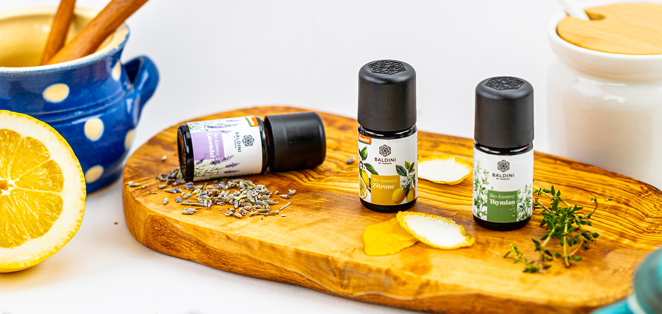 Baldini Bio-Essenzen Lavendel, Zitrone und Thymian auf einem Holzbrett, umgeben von Zitrone, Lavendel und frischen Kräutern.