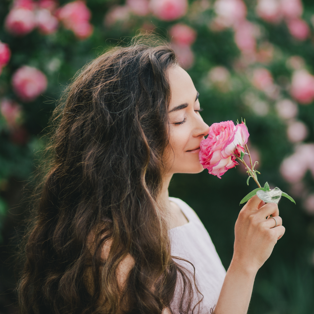 Frau mit langen Braunen Haaren riecht an einer  Rose