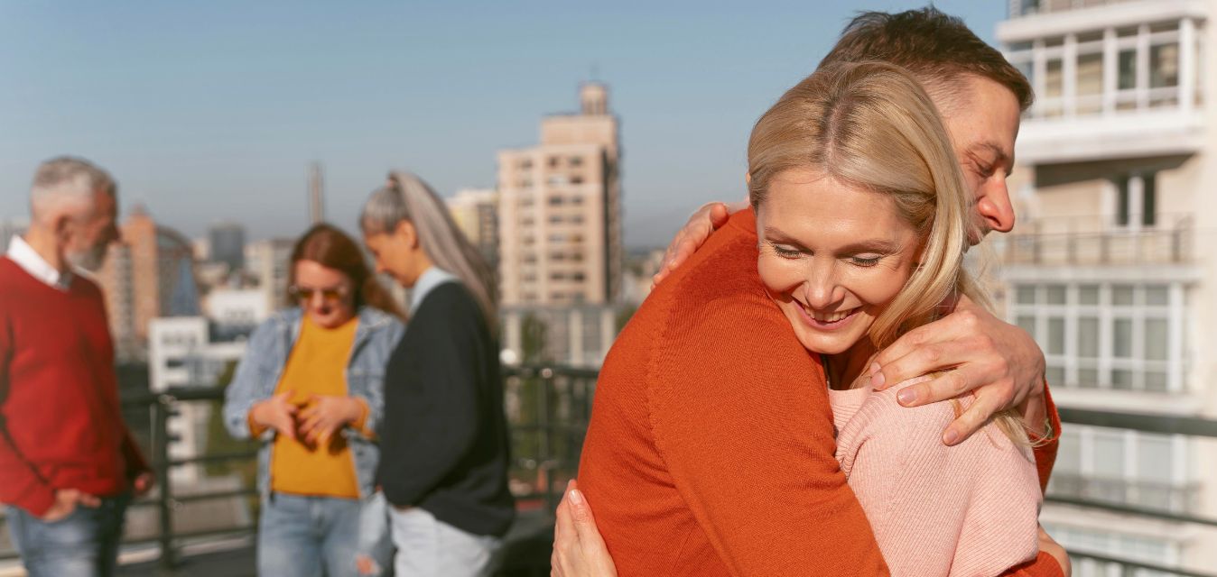 Menschen auf einer Dachterasse, drei unterhalten sich und zwei umarmen sich.