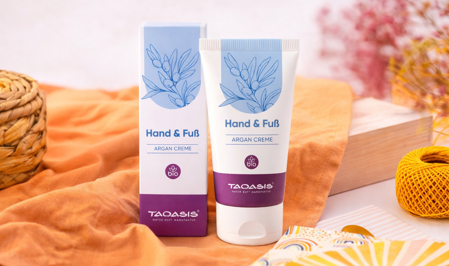 TAOASIS Hand & Fuß Argan Creme und Verpackung auf Stoff mit dekorativen Elementen in warmen Farben.