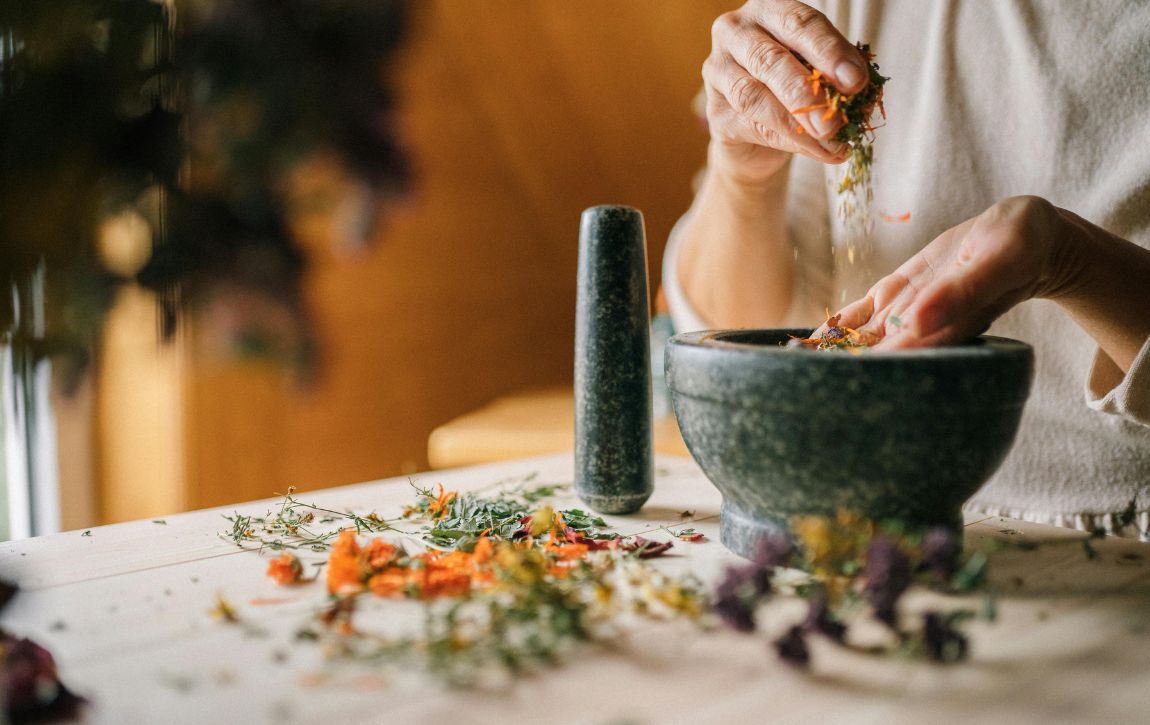 Mensch hat Kräuter in der Hand und sitzt am Tisch.