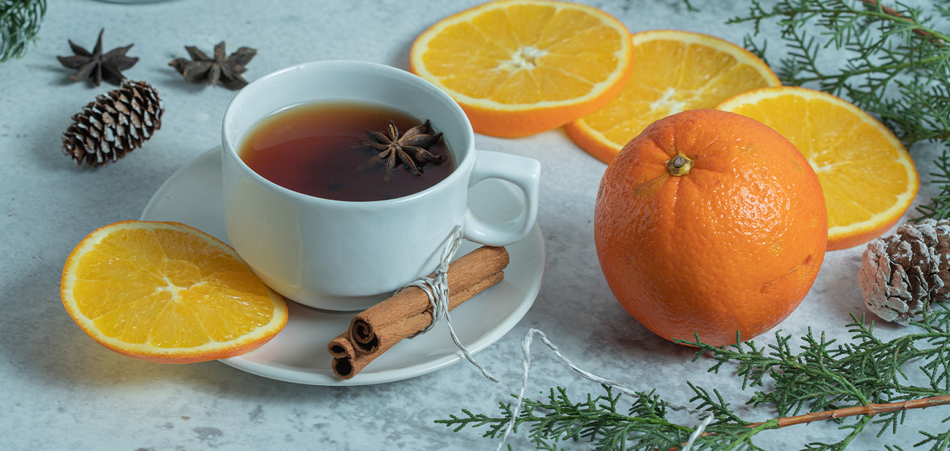 Tasse mit aromatischem Punsch, umgeben von Orangenscheiben, Zimtstangen, Sternanis und winterlichen Zweigen.