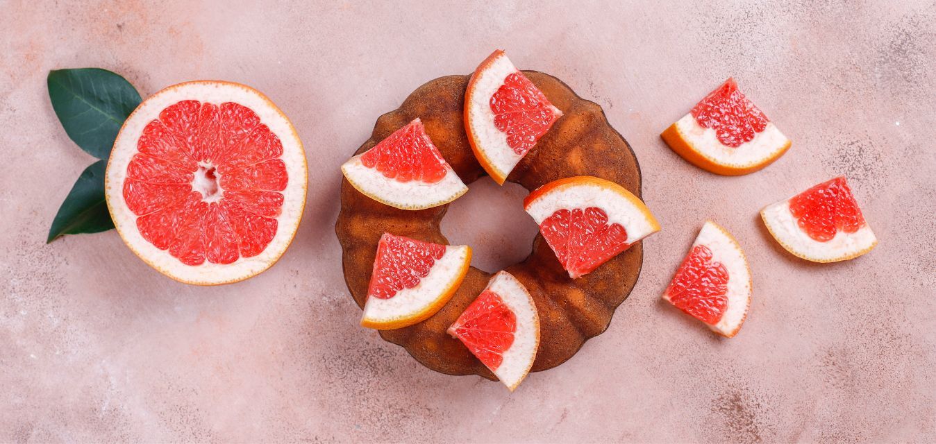 Gugelhupf mit frischen Grapefruitstücken und halbierter Grapefruit auf hellem Hintergrund.
