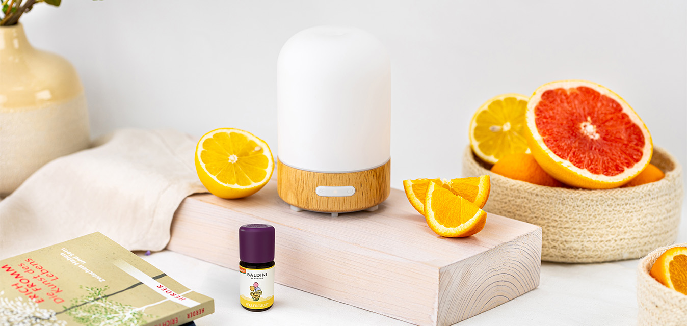 Weißer Aroma-Diffuser mit Baldini Feelfreude Duftkomposition, dekoriert mit Zitrone, Orange und Grapefruit auf hellem Hintergrund.
