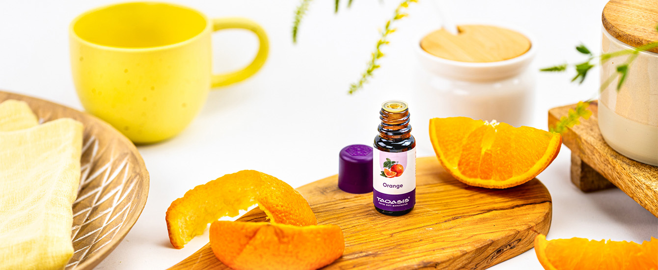 Orangenöl-Fläschchen mit violettem Deckel auf einem Holzbrett, umgeben von frischen Orangenspalten und Orangenschale.