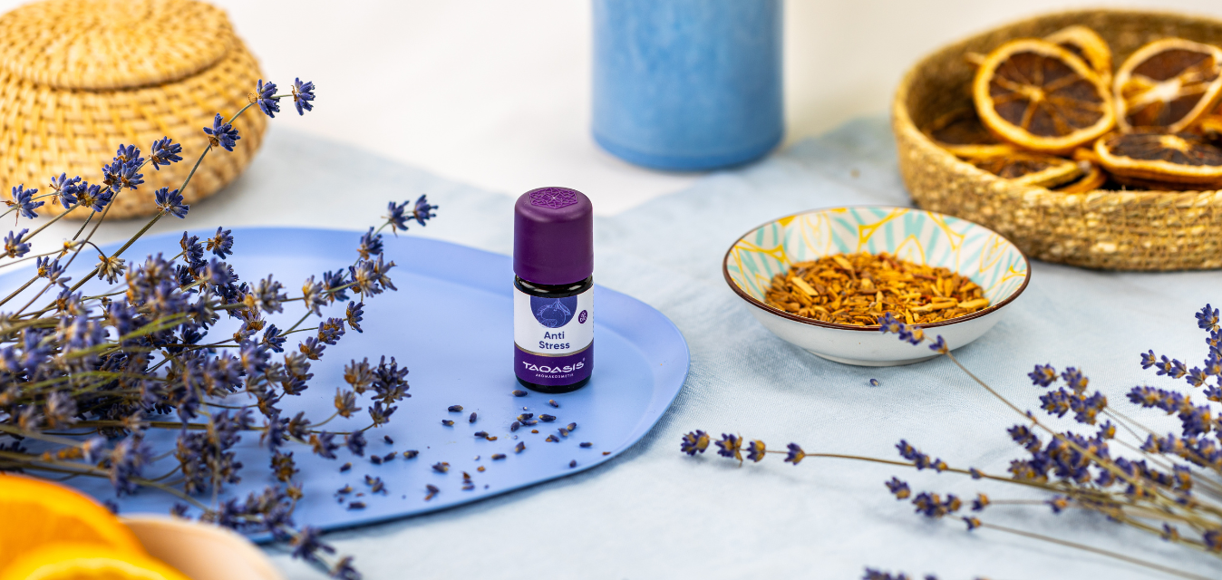 TAOASIS Anti-Stress Duftöl auf blauem Tablett, umgeben von Lavendelzweigen, getrockneten Blüten und Orangenscheiben in harmonischer Wellness-Atmosphäre.