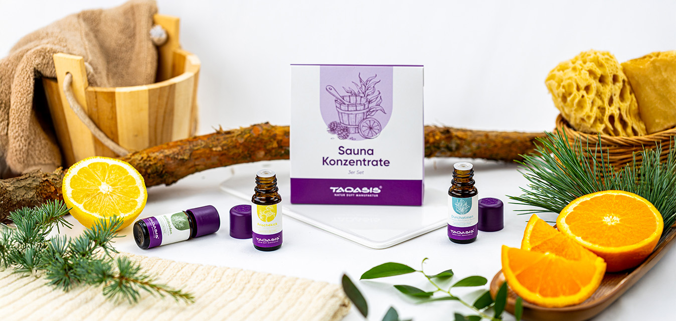 TAOASIS Sauna-Konzentrate mit ätherischen Ölen, dekoriert mit Zitrone, Orange, Tannenzweigen, Handtuch und Sauna-Zubehör.