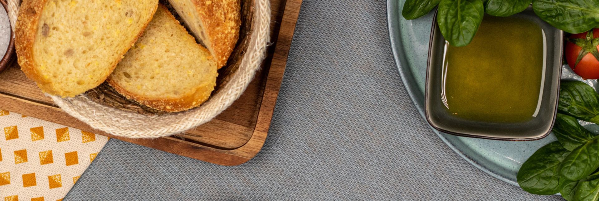 Frisches Brot mit Olivenöl, Basilikum und Tomaten auf gedecktem Tisch angerichtet.