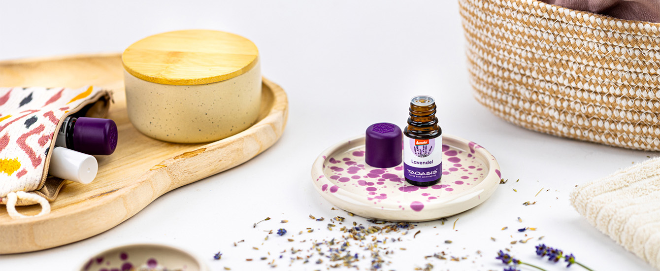 Lavendelöl-Fläschchen mit violettem Deckel auf einer Keramikschale, umgeben von getrocknetem Lavendel und natürlichen Wohnaccessoires.