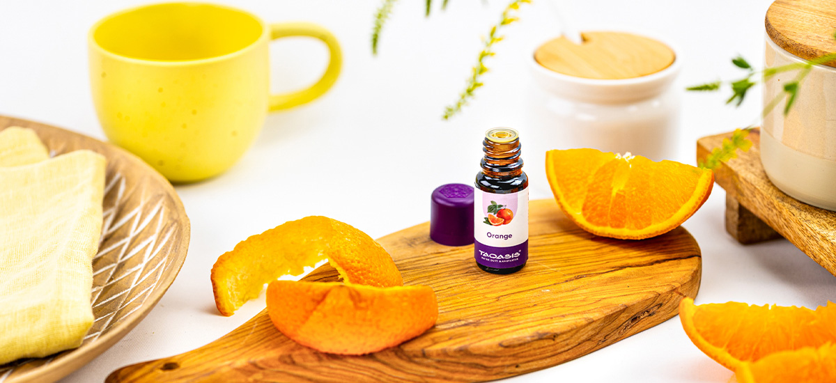 TAOASIS Orangenöl dekorativ mit frischer Orange und Orangenschalen auf einem Holzbrett arrangiert.